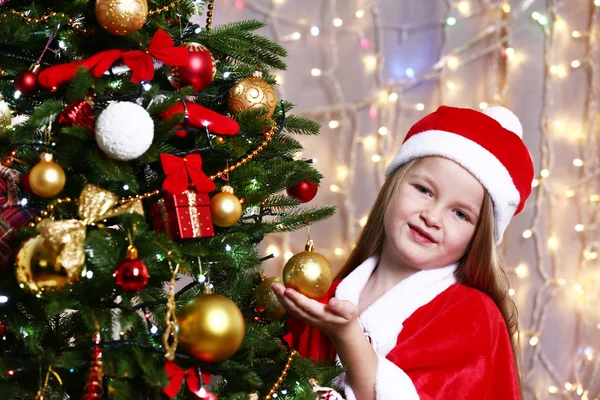 Little girl near Christmas tree on bright background — Stock Photo, Image