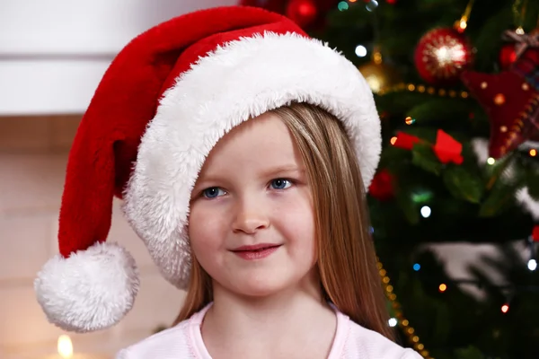 Bambina a Babbo Natale cappello vicino abete su sfondo camino — Foto Stock