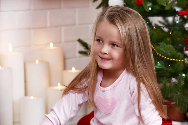 Little girl sitting near fir tree on fireplace with candles background — Stockfoto