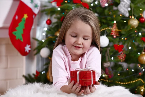 Kleines Mädchen liegt mit Geschenk auf Fellteppich auf Christbaumhintergrund — Stockfoto