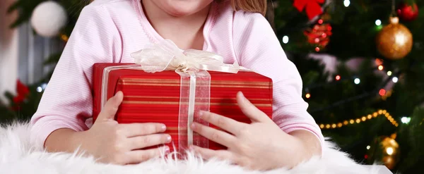 Little girl lying with gift on fur carpet on Christmas tree background — ストック写真