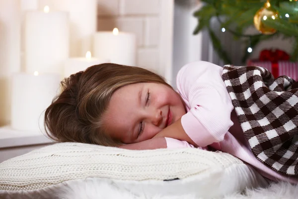 Little girl sleeping on fur carpet on fir tree and fireplace with candles background — Stok fotoğraf