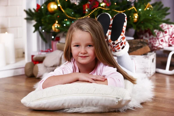 Little girl lying on fur carpet and wooden floor on Christmas tree background — Φωτογραφία Αρχείου