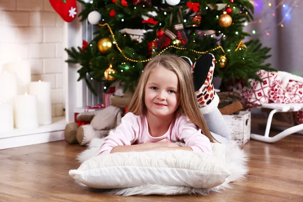 Little girl lying on fur carpet and wooden floor on Christmas tree background — Stok fotoğraf