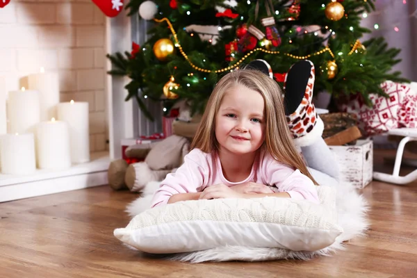 Little girl lying on fur carpet and wooden floor on Christmas tree background — Stock fotografie