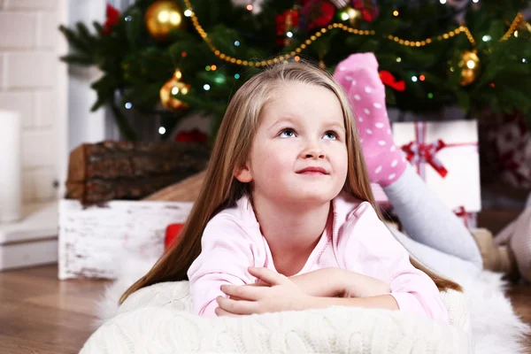 Little girl lying on fur carpet and wooden floor on Christmas tree background — Stok fotoğraf