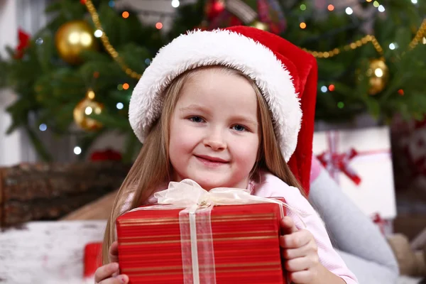 Little girl in Santa hat lying on fur carpet on Christmas tree background — Zdjęcie stockowe