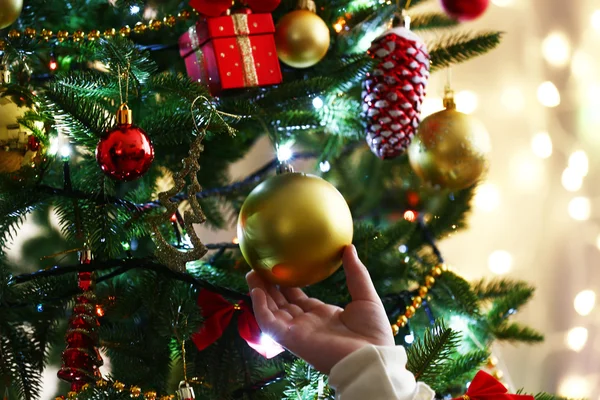 Child's hands hanging bauble on Christmas tree on bright background — ストック写真