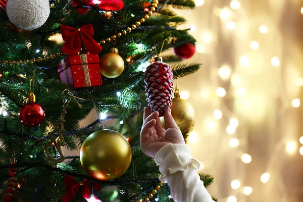 Child's hands hanging bauble on Christmas tree on bright background — ストック写真