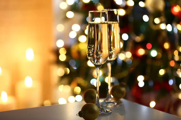 Two glass with champagne with chocolates and baubles on table on Christmas tree and fireplace background — Stok fotoğraf