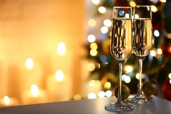 Dois copos com champanhe com chocolates e bugigangas na mesa na árvore de Natal e fundo da lareira — Fotografia de Stock