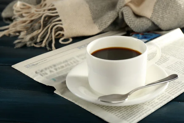 Tasse Kaffee mit Untertasse und Löffel auf Zeitungspapier auf farbigem Holzhintergrund — Stockfoto