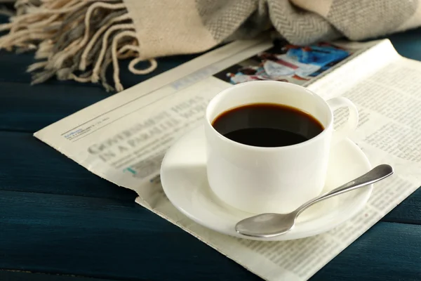 Tasse Kaffee mit Untertasse und Löffel auf Zeitungspapier auf farbigem Holzhintergrund — Stockfoto