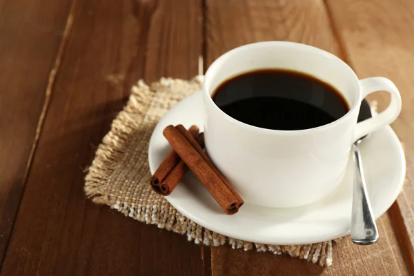 Tasse de café avec soucoupe, cuillère et cannelle sur fond de table en bois — Photo