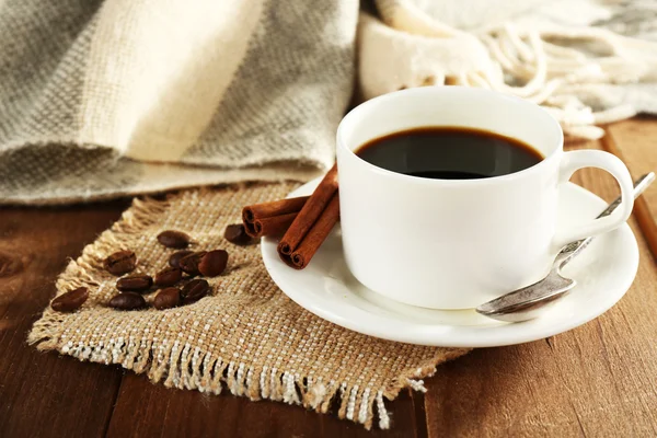 Cup of coffee with coffee beans and cinnamon on burlap cloth on wooden table background — Stock Photo, Image