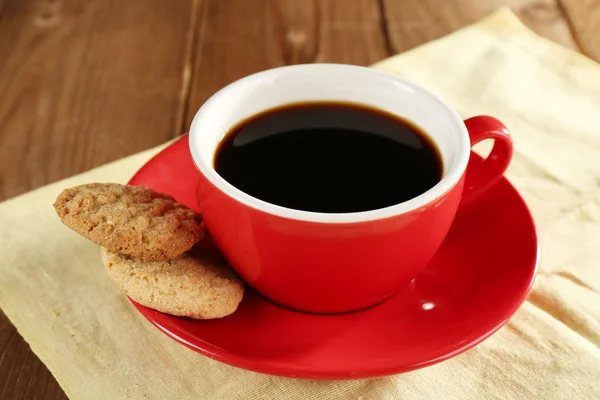 Cup of coffee on saucer with cookies on color napkin on wooden table background — Stock fotografie