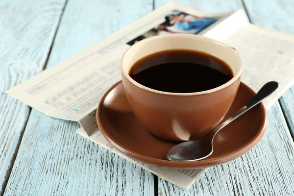 Cup of coffee with newspaper on color wooden background — Stock Photo, Image