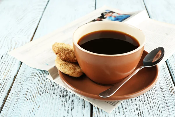 Cup of coffee with newspaper on color wooden background — Stock Photo, Image