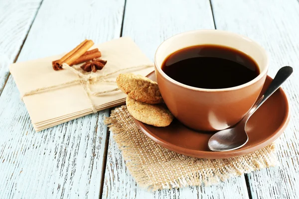 Cup of coffee with spoon and cookies on burlap cloth near envelopes on color wooden background — Stock fotografie