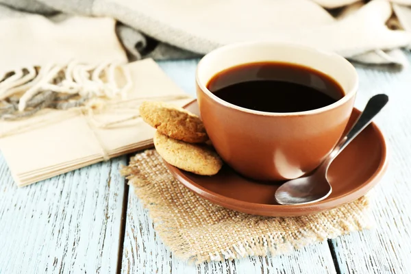 Taza de café con cuchara y galletas sobre tela de arpillera cerca de sobres sobre fondo de madera de color — Foto de Stock
