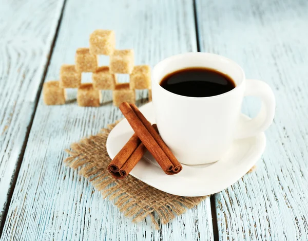 Cup of coffee on burlap cloth with coffee beans on color wooden background — Zdjęcie stockowe