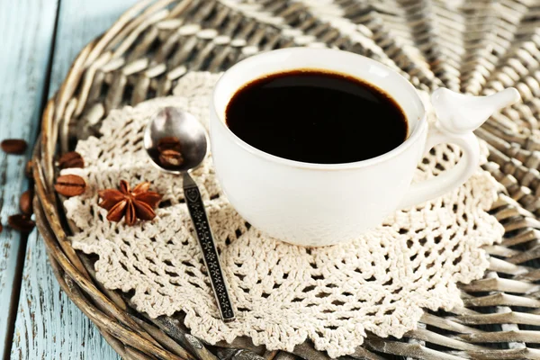 Cup of coffee with lace doily, spoon and coffee beans on wicker stand, on color wooden background — Stock Photo, Image