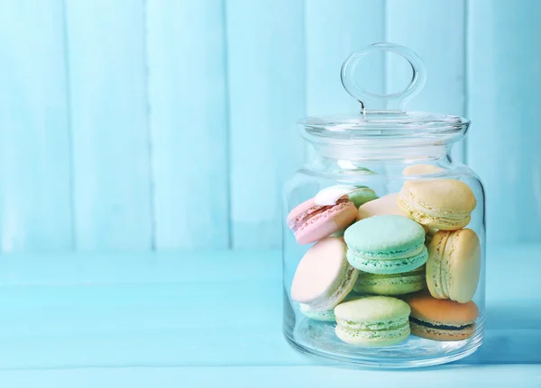 Gentle colorful macaroons in glass jar on color wooden table background — Stock fotografie