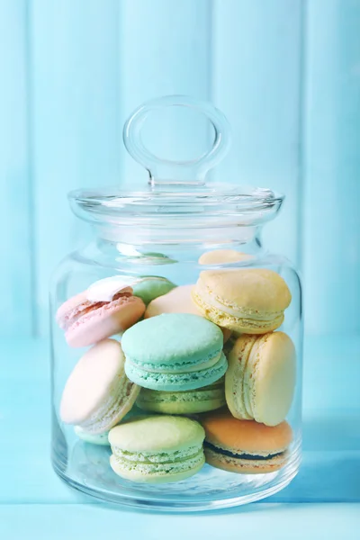 Gentle colorful macaroons in glass jar on color wooden table background — Stockfoto
