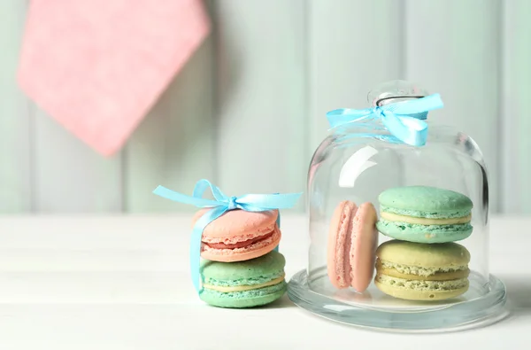 Gentle colorful macaroons in glass bell jar on color wooden table background — Stock Photo, Image