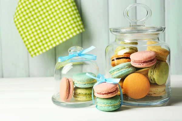 Gentle colorful macaroons in glass jars on color wooden table background — Stockfoto