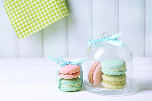 Gentle colorful macaroons in glass bell jar on color wooden table background — Zdjęcie stockowe