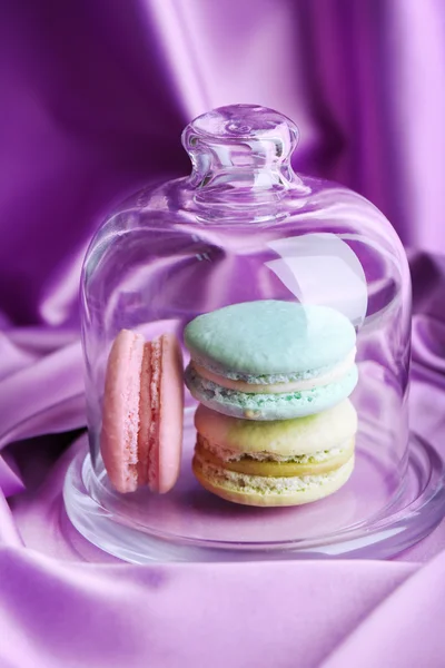 Macaroons coloridos suaves no frasco de sino de vidro no fundo de tecido de cor — Fotografia de Stock