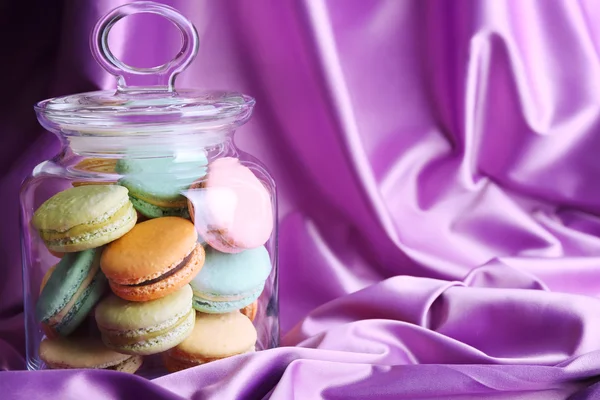 Macarons colorés doux dans un bocal en verre sur fond de tissu couleur — Photo