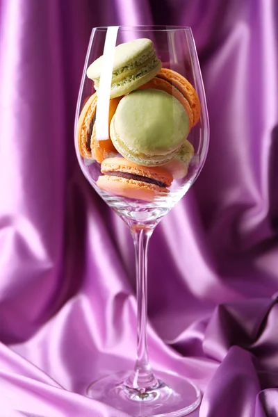 Macaroons coloridos suaves em vidro de vinho no fundo de tecido de cor — Fotografia de Stock