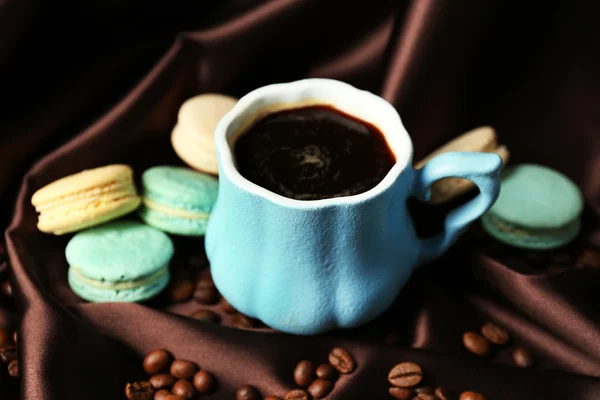 Gentle colorful macaroons and black coffee in mug on color fabric background — Stock Photo, Image