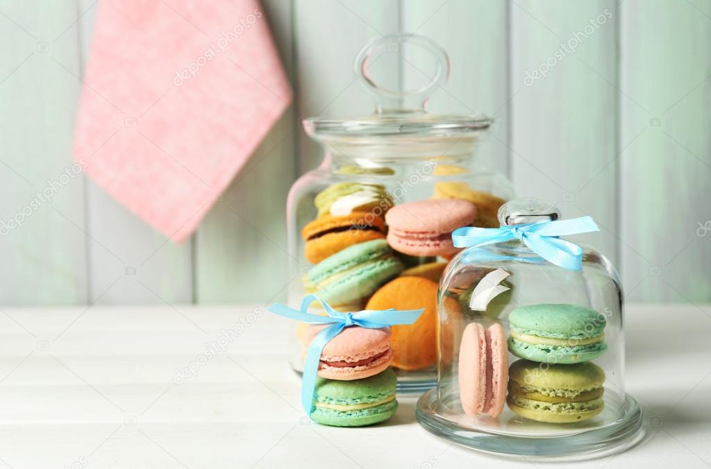 Gentle colorful macaroons in glass jars on color wooden table background