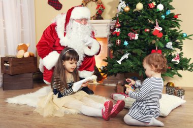 Noel Baba ile iki küçük sevimli kız şömine ve Noel ağacı evde yakınındaki