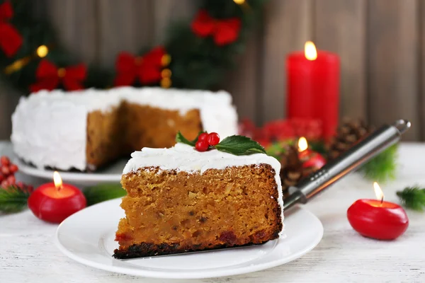 Slice of cake covered cream with Christmas decoration on table, on wooden wall background — Stock Photo, Image