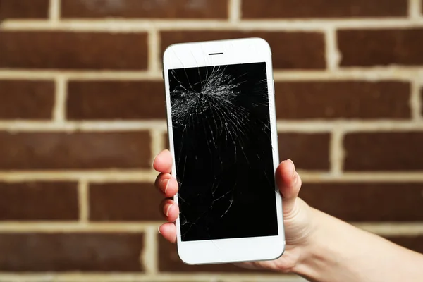 Broken iPhone in hand on brick background