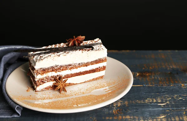 Gâteau tiramisu savoureux sur assiette, sur table en bois, sur fond noir — Photo