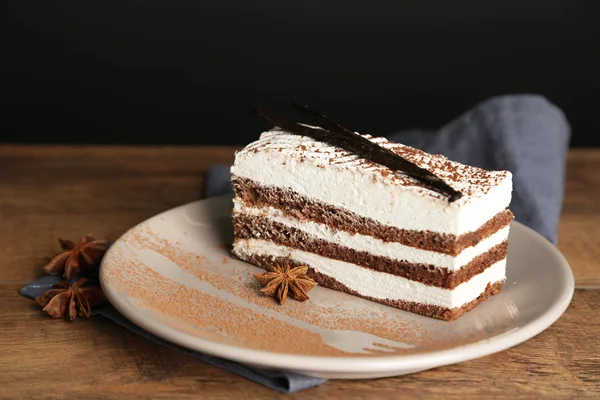 Gustosa torta tiramisù su piatto, su tavolo di legno, su fondo nero — Foto Stock