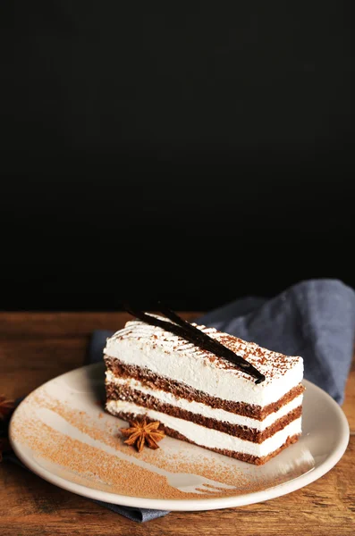 Leckerer Tiramisu-Kuchen auf Teller, auf Holztisch, auf schwarzem Hintergrund — Stockfoto
