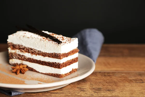 Gustosa torta tiramisù su piatto, su tavolo di legno, su fondo nero — Foto Stock