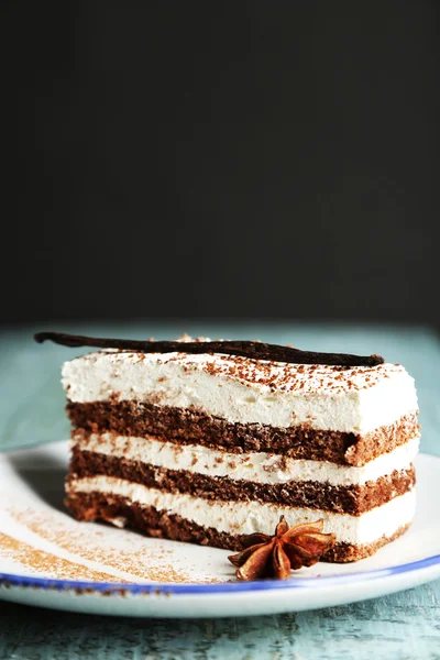 Tasty tiramisu cake on plate, on wooden table, on black background — Stock Photo, Image