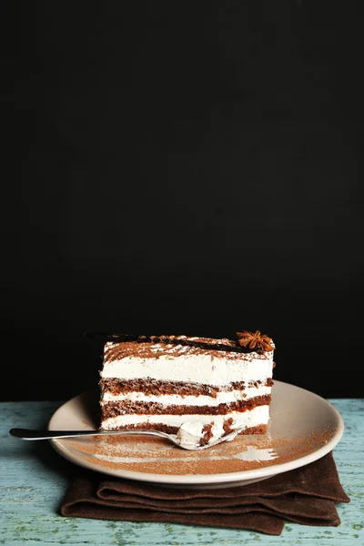 Leckerer Tiramisu-Kuchen auf Teller, auf Holztisch, auf schwarzem Hintergrund — Stockfoto