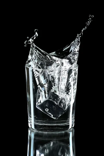 Water splash met ijs in glas geïsoleerd op zwart — Stockfoto