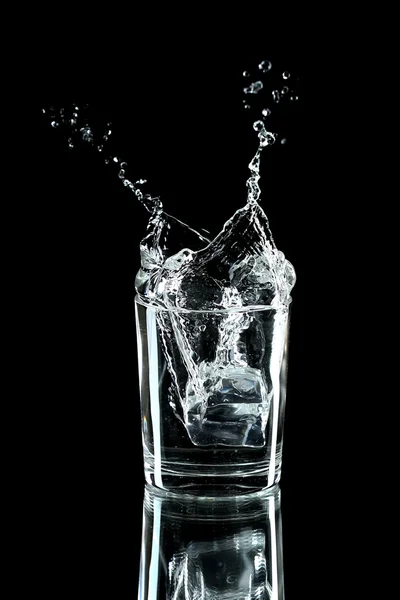 Salpicadura de agua con hielo en vidrio aislado en negro —  Fotos de Stock