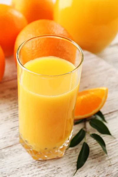 Vaso de jugo de naranja y naranjas sobre fondo de mesa de madera de color — Foto de Stock