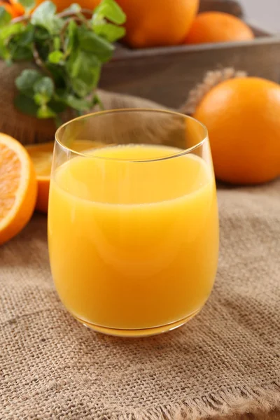 Glass of orange juice on wooden table with burlap cloth background — Stock Photo, Image