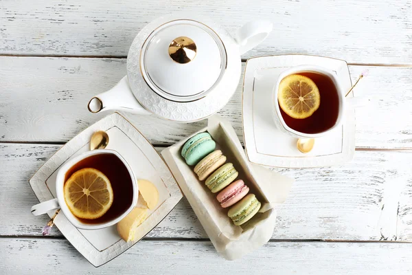 Bunte Makronen mit Teekanne und Tasse Tee auf farbigem Holzhintergrund — Stockfoto